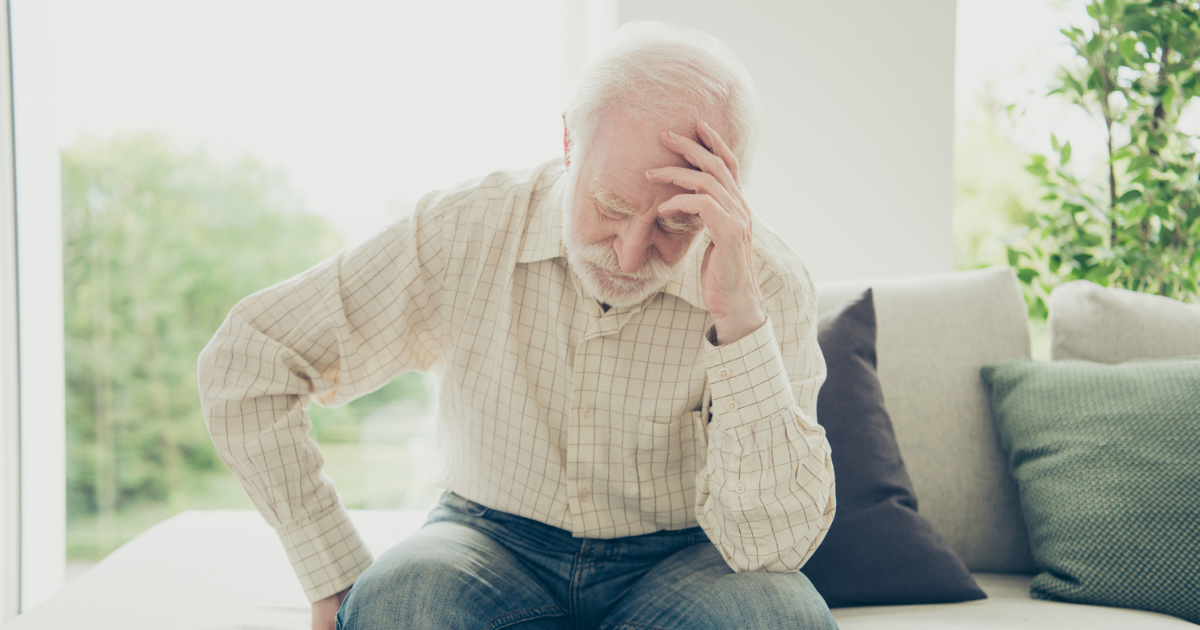 Older man sitting on the couch holding his head