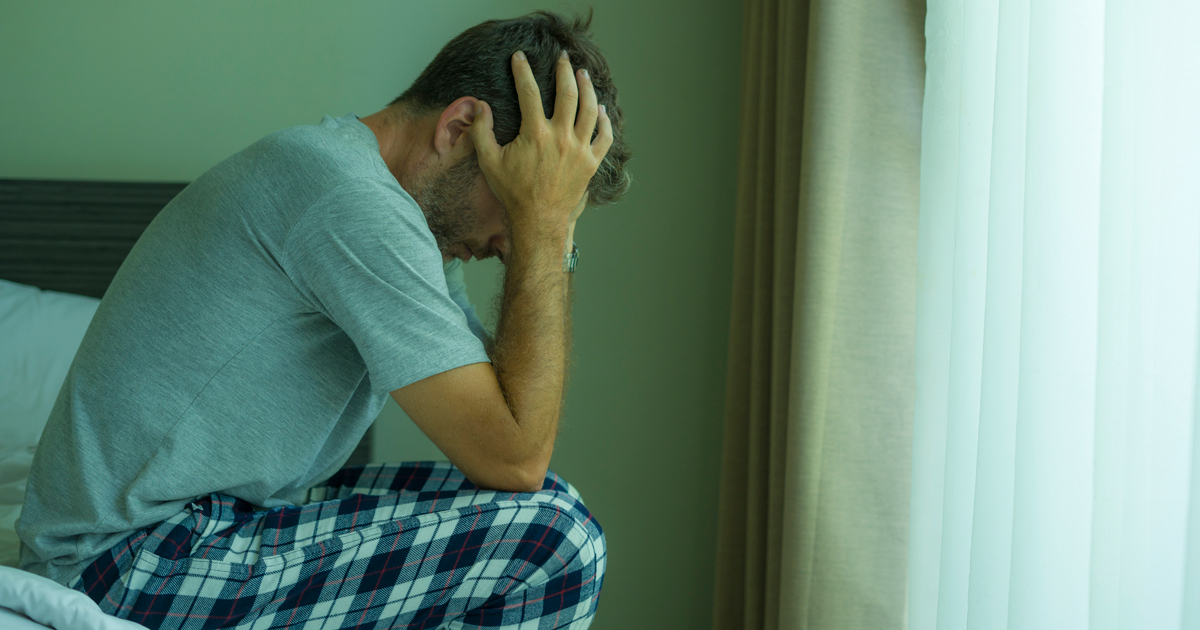 picture of a man sitting in bed with his head in his hands