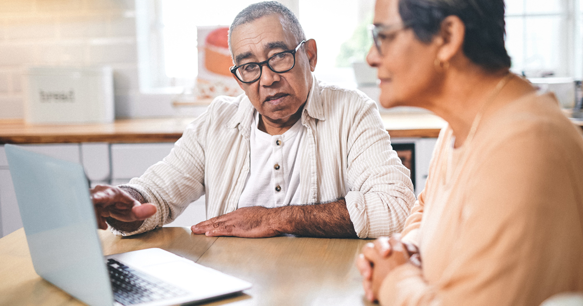 An older man and woman seated at a table looking at a laptop