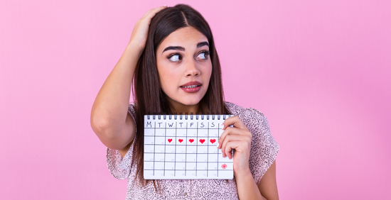 A woman with an uncertain face, holding up a calendar with red hearts marking that days of a period.