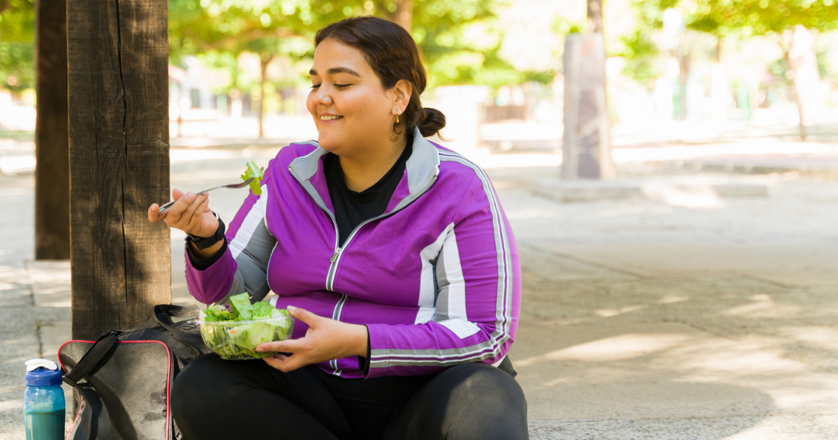 Woman sitting on the sidewalk and eating a salad