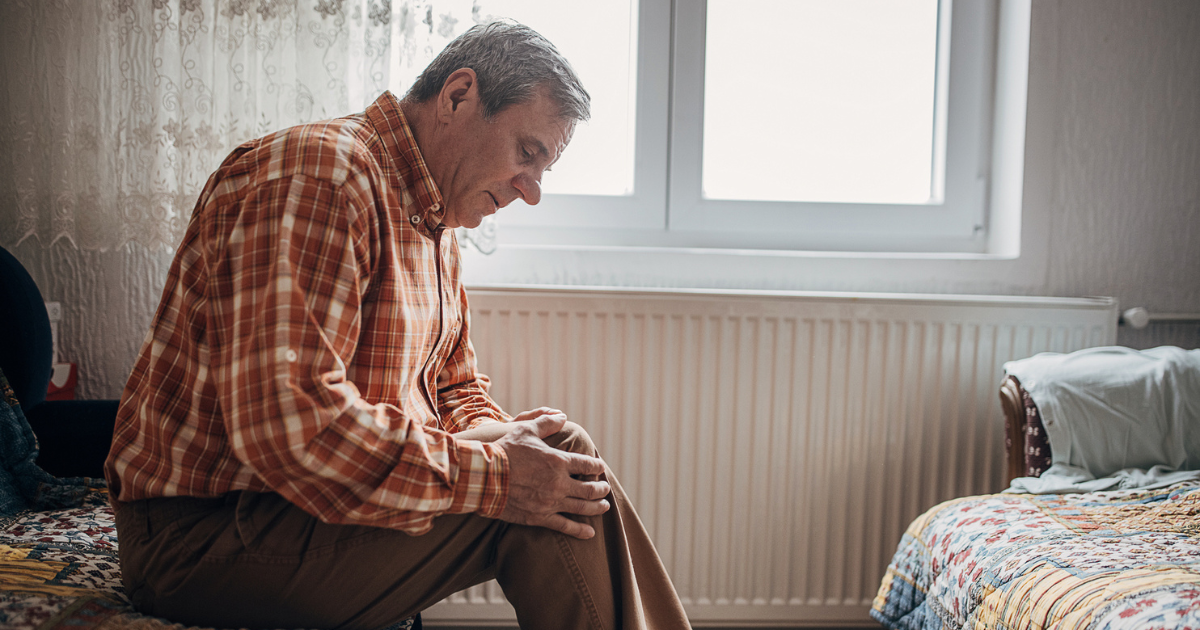 Older man sitting on a bed, holding his knee