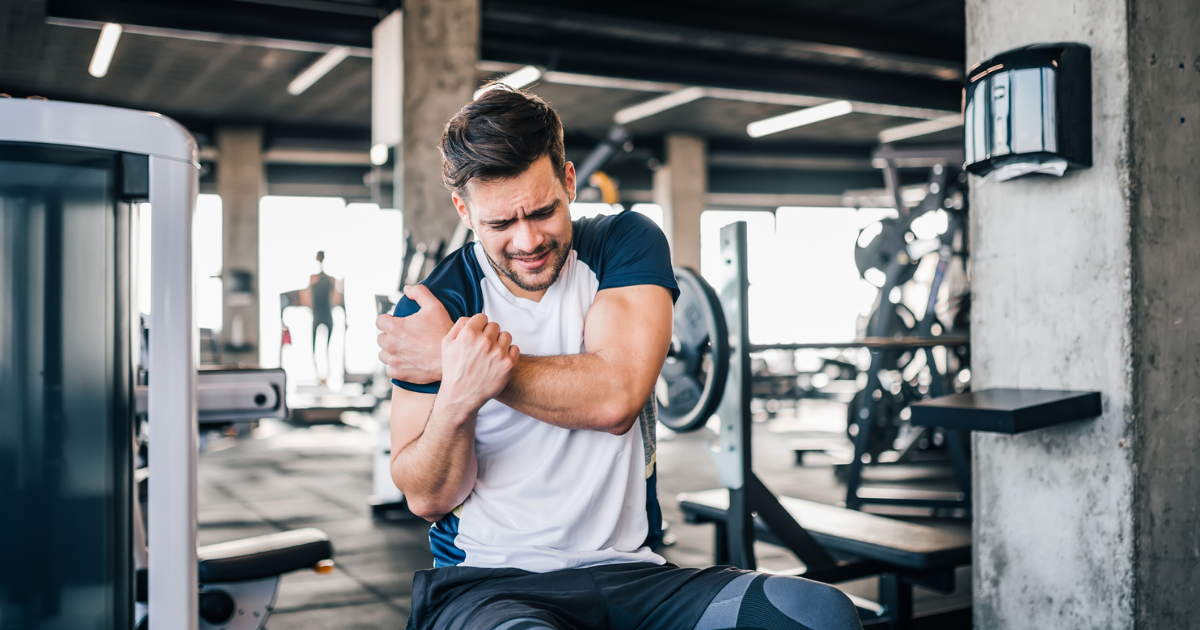 Man sitting on a weight bench and holding his shoulder in pain