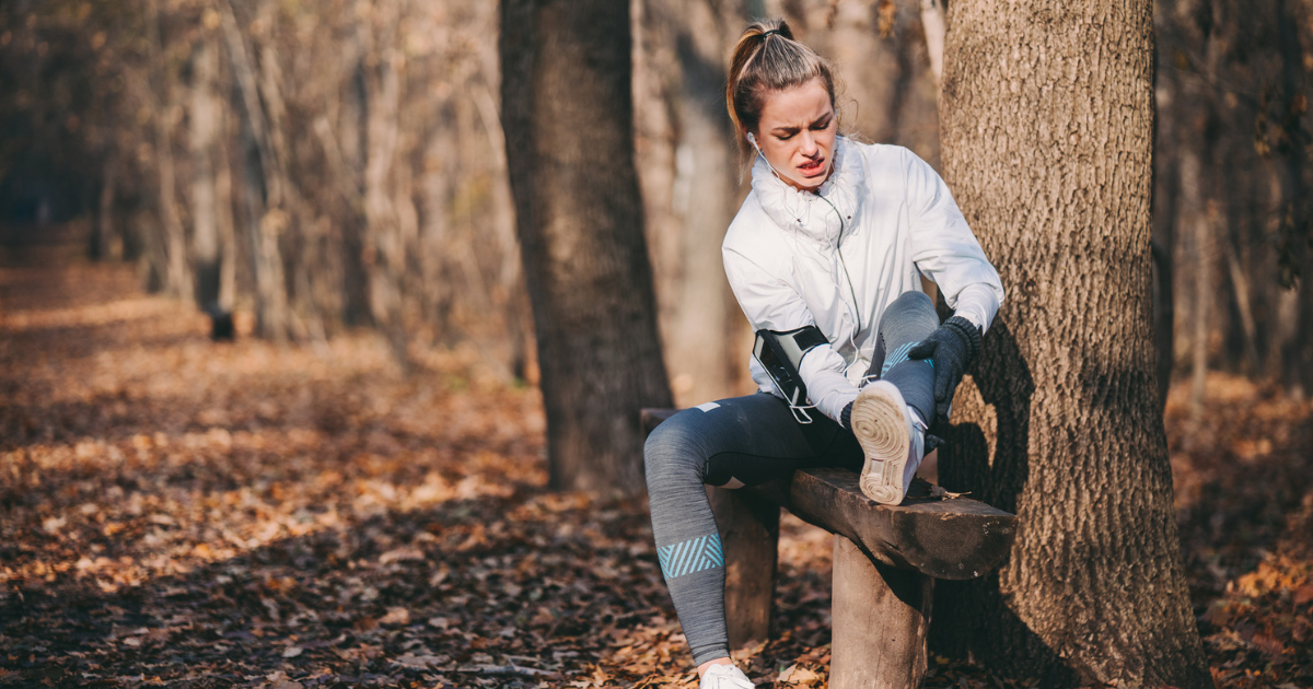 Woman sitting on a bench in the woods, holding her ankle