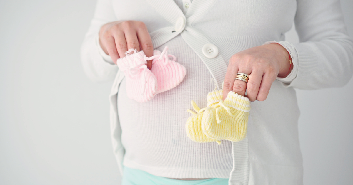 Pregnant woman holding two sets of booties in front of her stomach