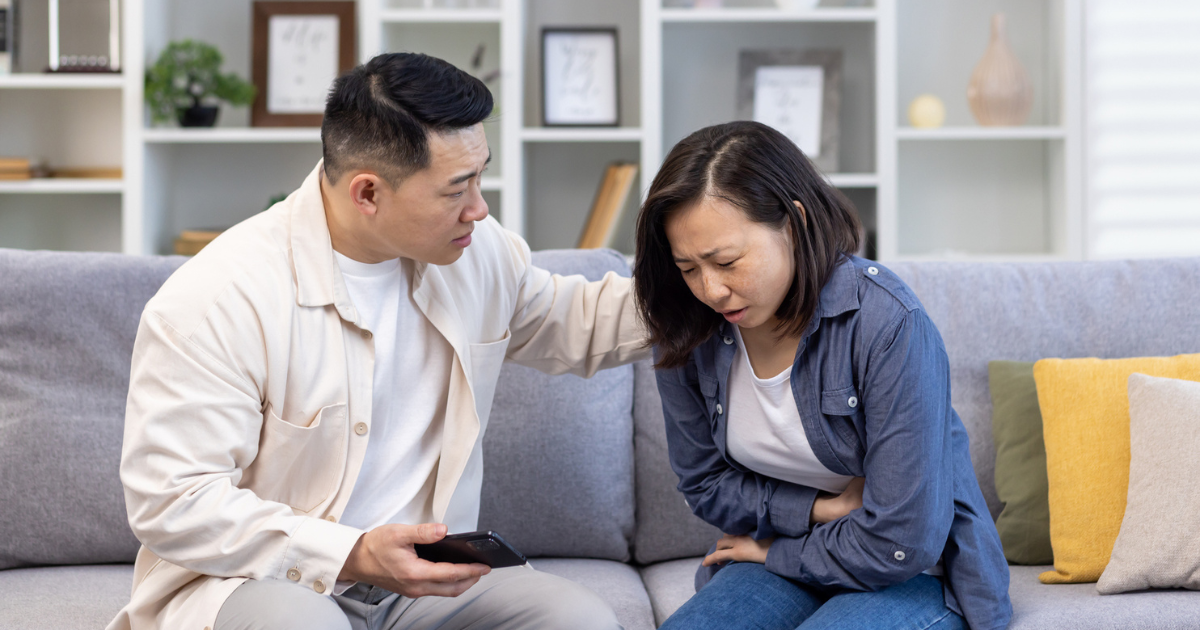 Woman holding her stomach in pain sitting on the couch with a man