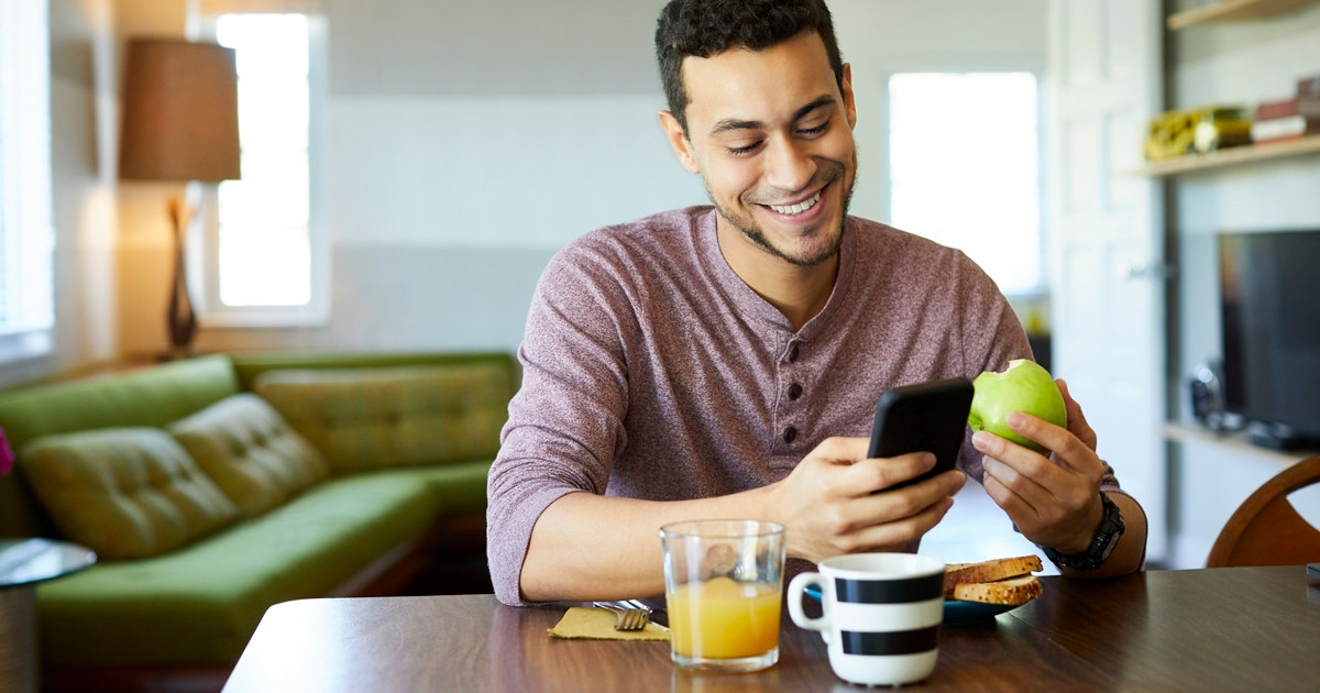 Man eating apple while looking at phone