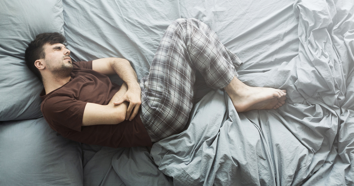 Man laying in bed holding his stomach in pain