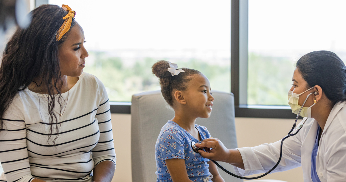 Mother and young daughter in doctor's office, doctor using stethoscope on daughter