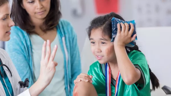 Young girl in a soccer uniform holding an ice pack against her head while a doctor holds up three fingers