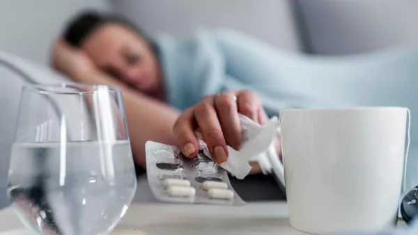 Sick woman laying on the couch, reaching for medicine