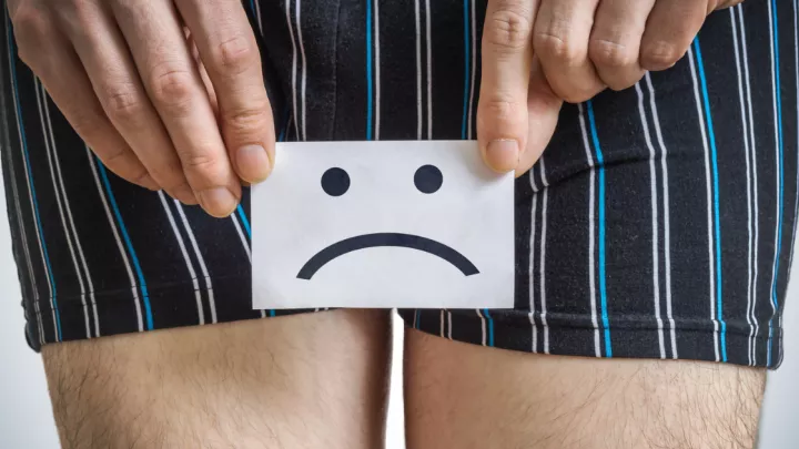 Sad face drawn on a piece of paper, held in front of a man's waist