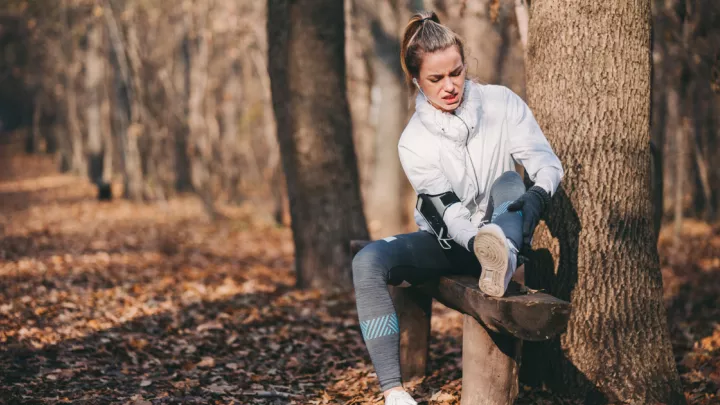 Woman sitting on a bench in the woods, holding her ankle