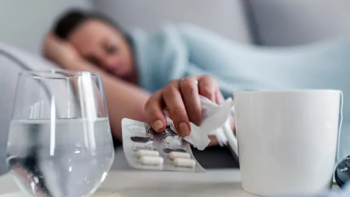 Sick woman laying on the couch, reaching for medicine