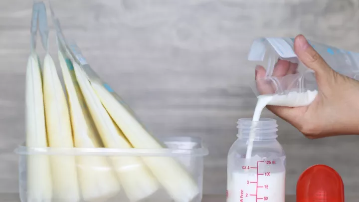 Close up of a hand pouring breast milk from a storage bag into a baby bottle