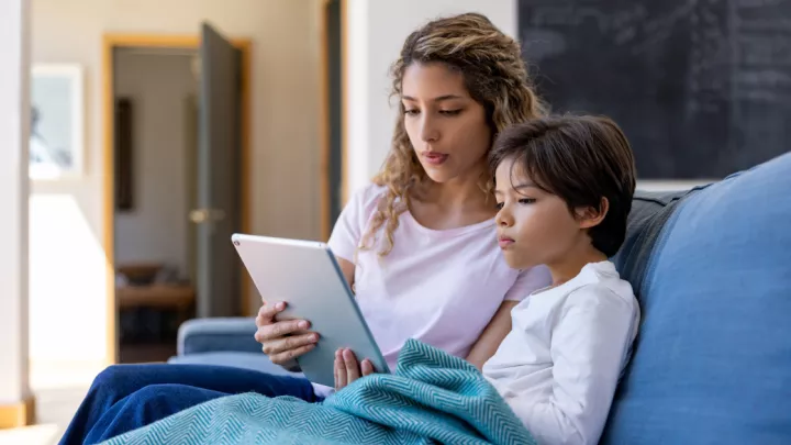 Mother and young son sitting on couch using a tablet for a telehealth appointment
