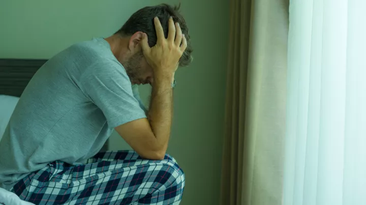 picture of a man sitting in bed with his head in his hands