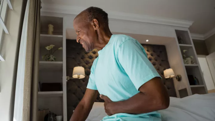 Older man sitting on his bed holding his stomach