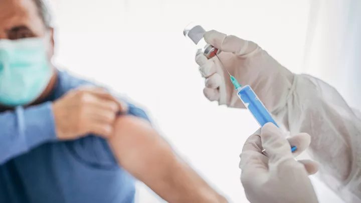 picture of a man in a mask rolling up his sleeve for his vaccination