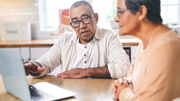 An older man and woman seated at a table looking at a laptop