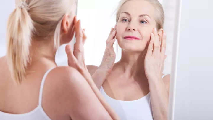 Woman looking at skin in mirror.