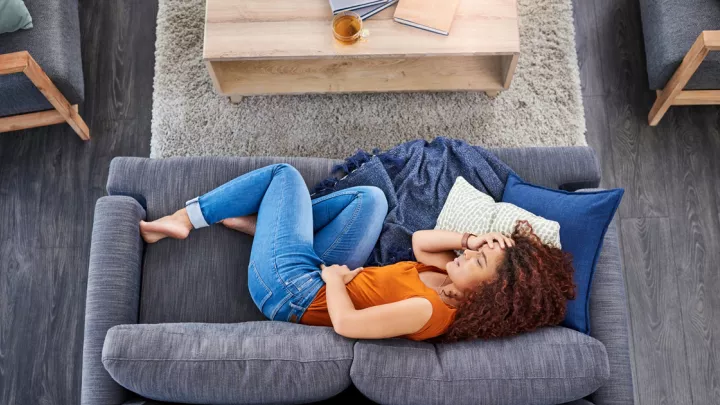 Woman holding her stomach laying on her couch