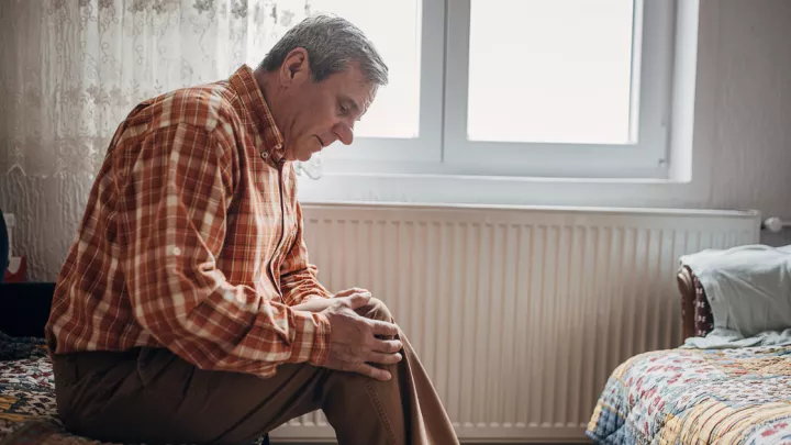 Older man sitting on a bed, holding his knee