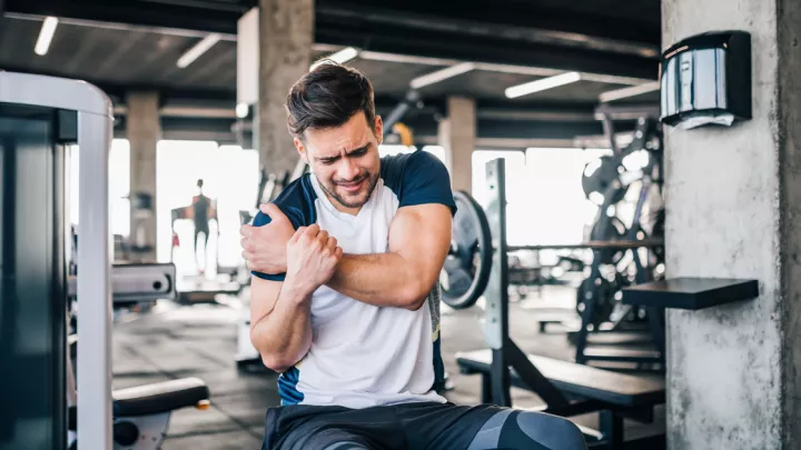 Man sitting on a weight bench and holding his shoulder in pain