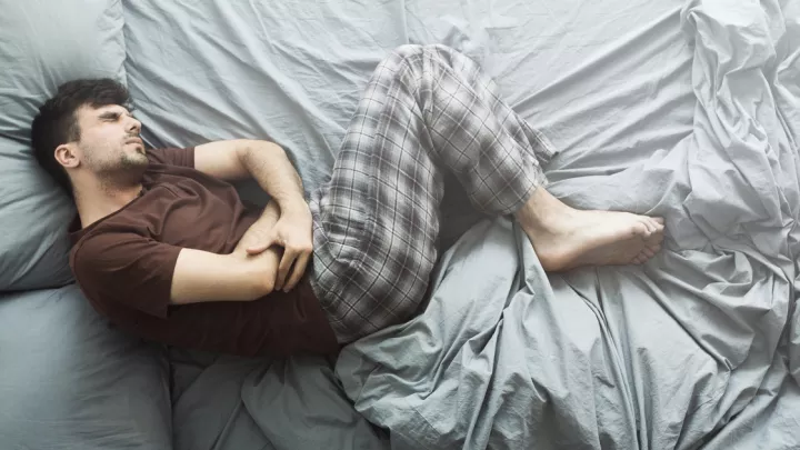 Man laying in bed holding his stomach in pain