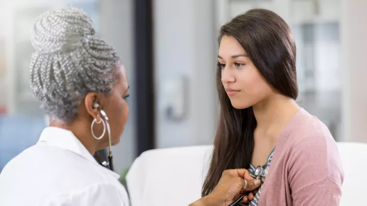 Doctor listening to the heartbeat of a young woman with a stethoscope 