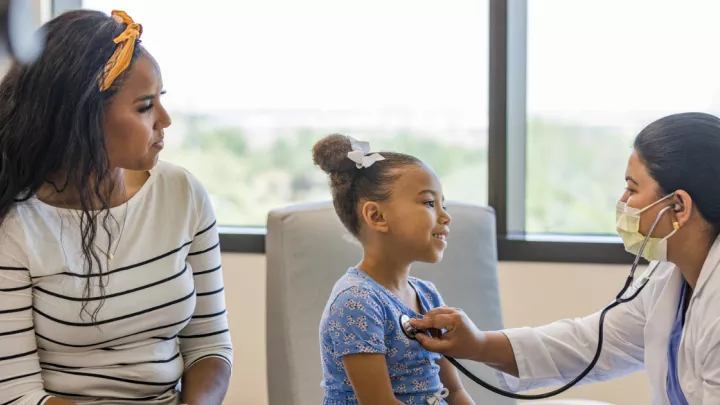 Mother and young daughter in doctor's office, doctor using stethoscope on daughter