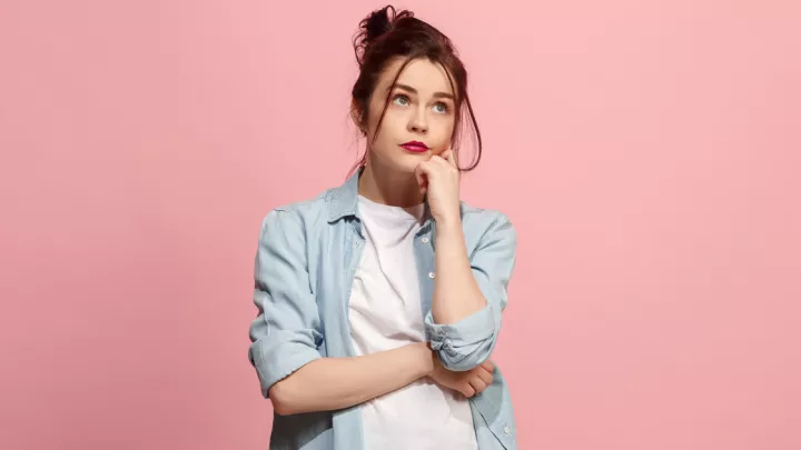 Young woman holding her chin against a pink background